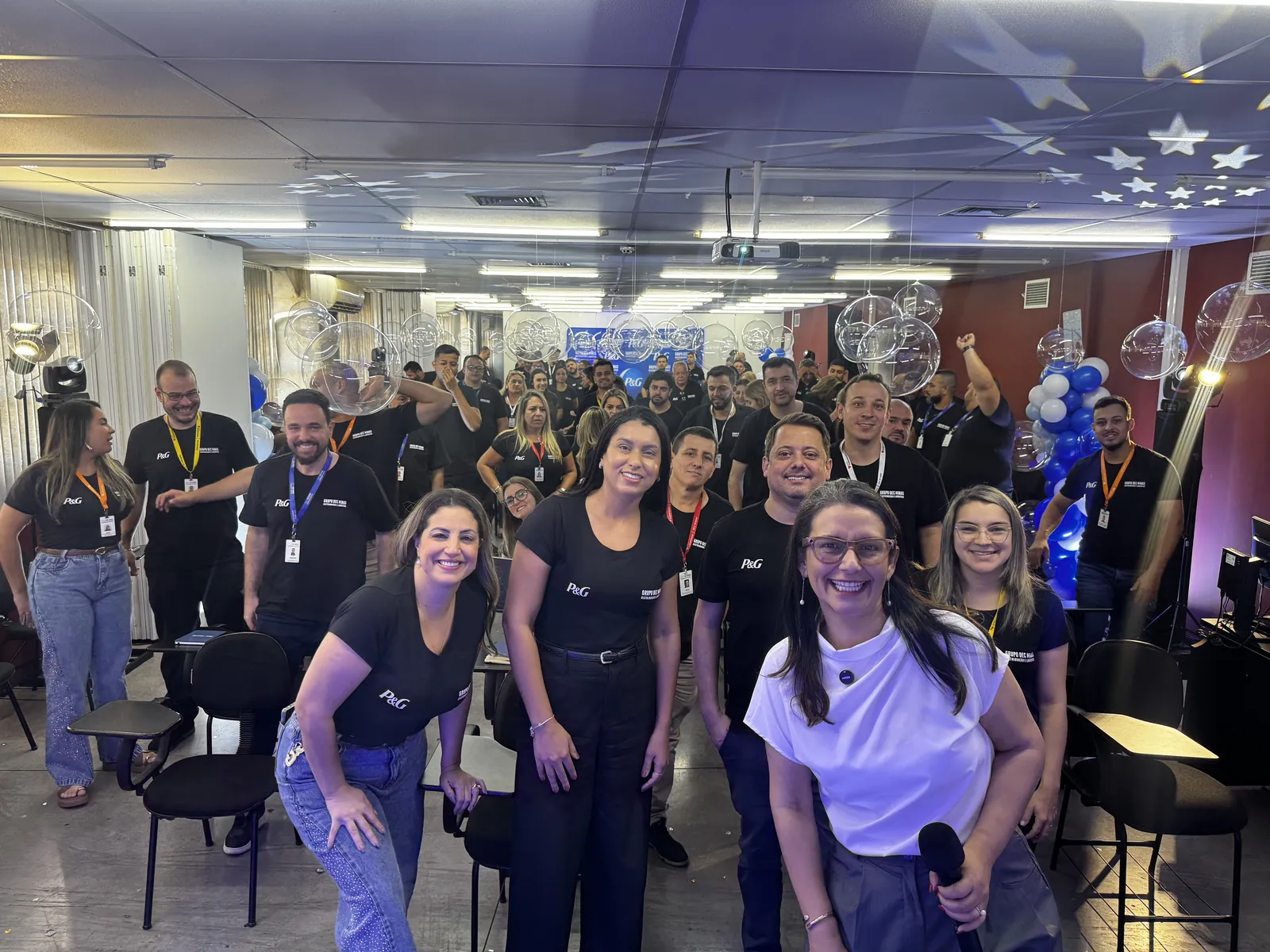Carol Villaça sorrindo com o microfone na mão, na frente da plateia inteira de uma convenção de vendas