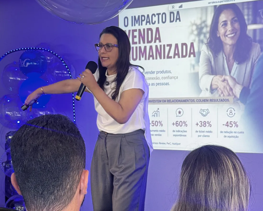 Carol Villaça com o microfone, apontando para a plateia durante a palestra